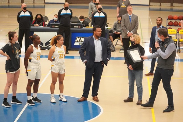 Baltimore County Executive John Olszewski Jr. (far right) reads citation of achievement he bestowed on the Knights women's basketball team, as CCBC President Sandra L. Kurtinitis (to left of Olszewski), head coach Mike Seney (center), and captains Kendal Haggerty, Patricia Anumgba, and Lyric Swann (left to right) watch on.
